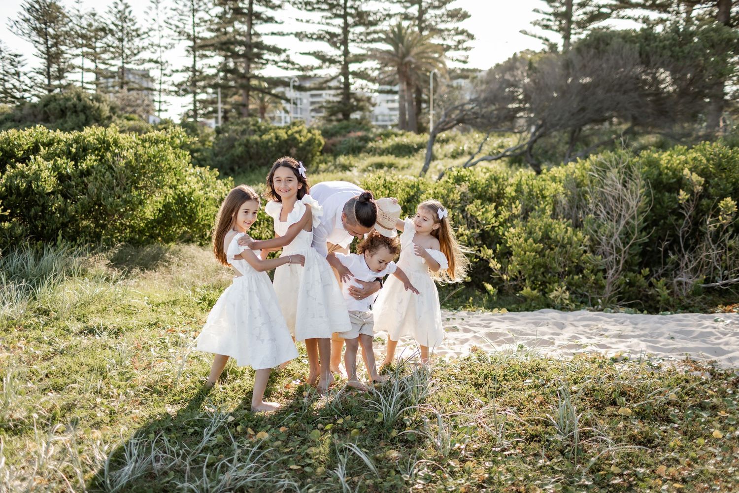 Group in white dresses walking together through coastal landscape with pine trees.