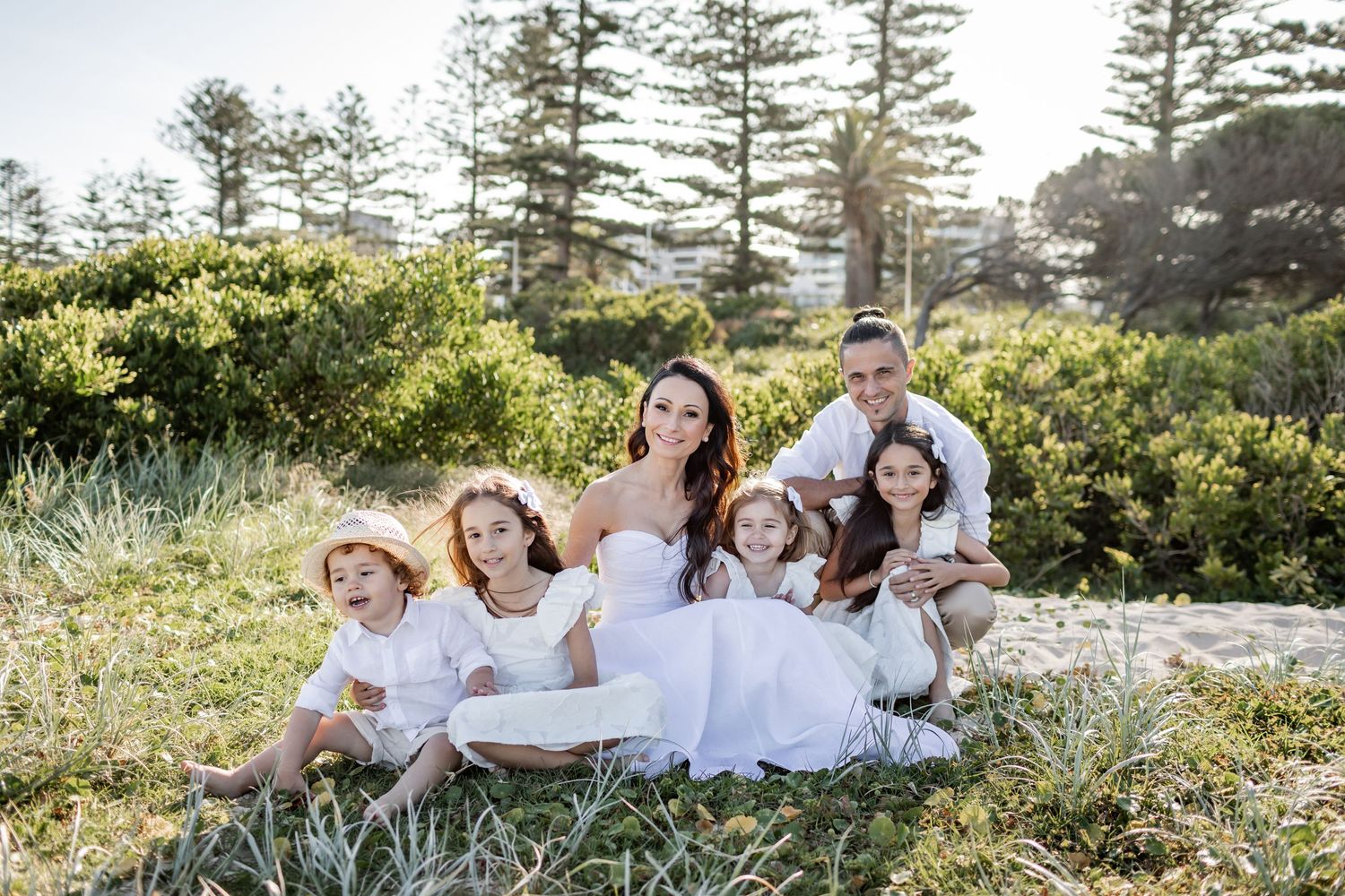 A family in white clothing poses together on grassy coastal terrain.