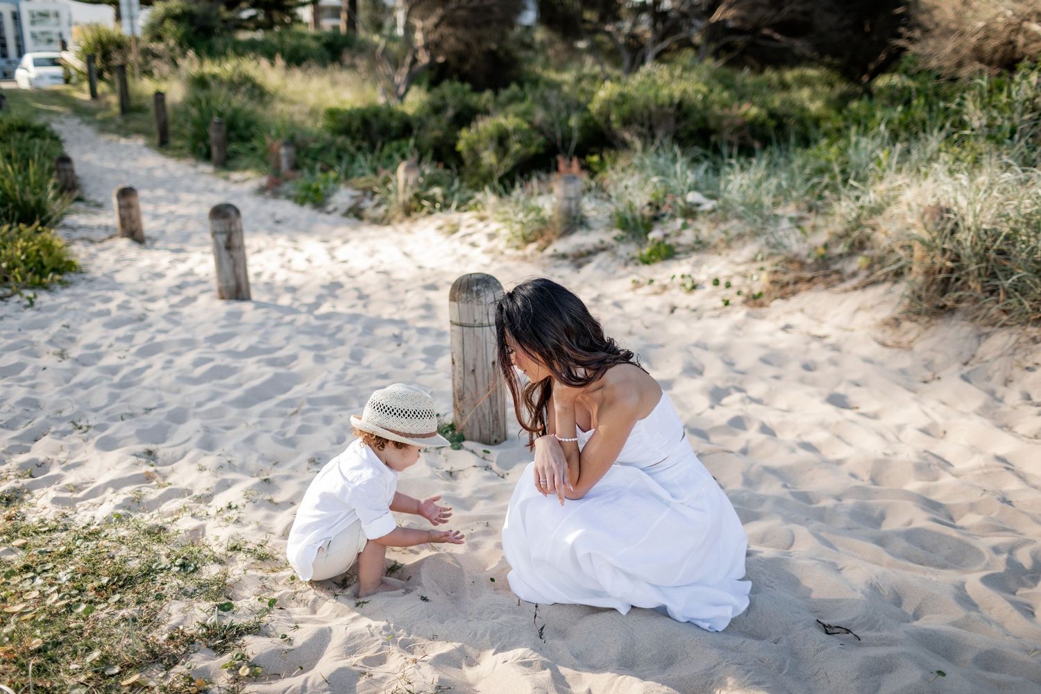 Two people in white dresses sitting together on sandy beach path.