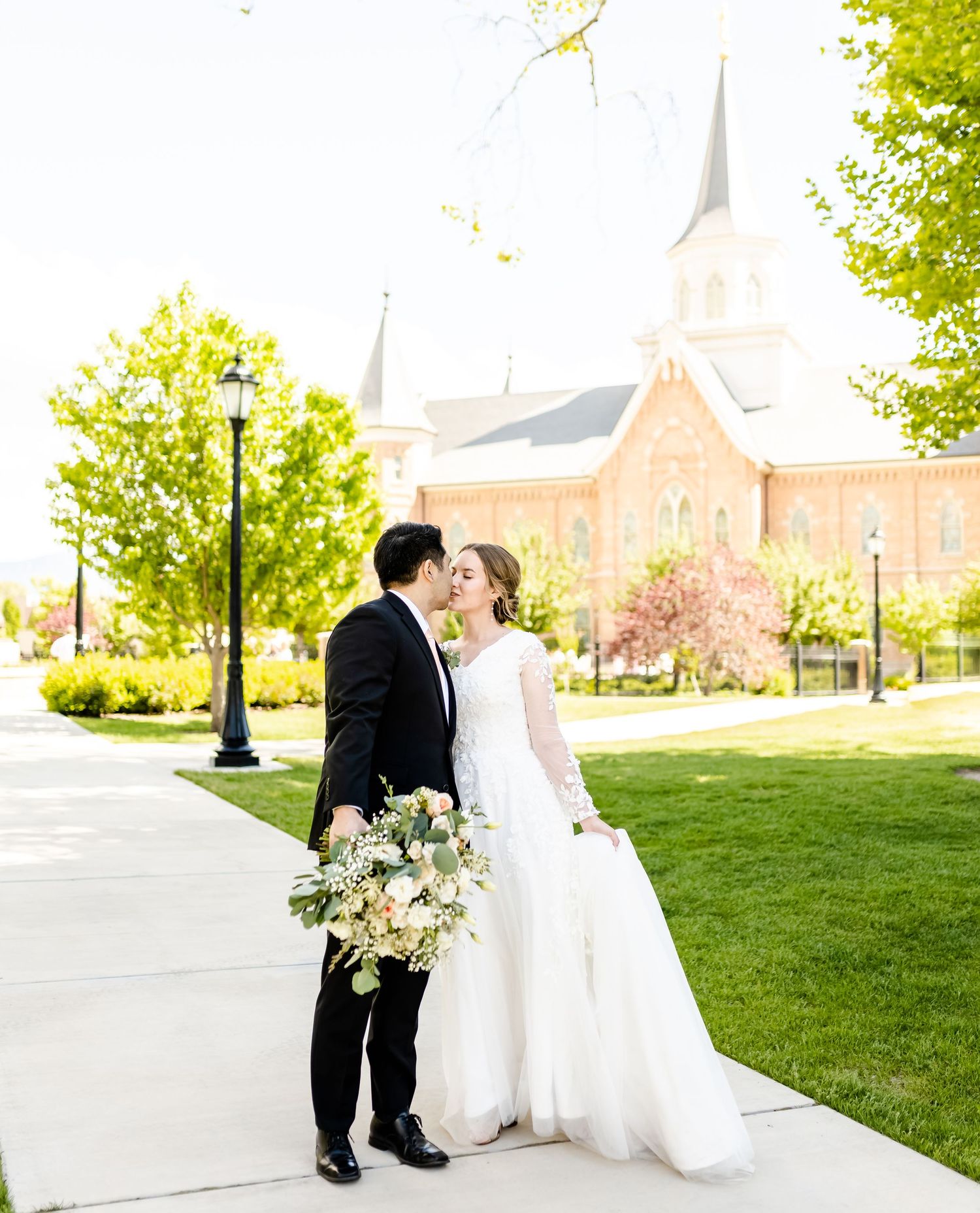 A wedding couple poses for romantic portraits outside a beautiful brick church with white spires.