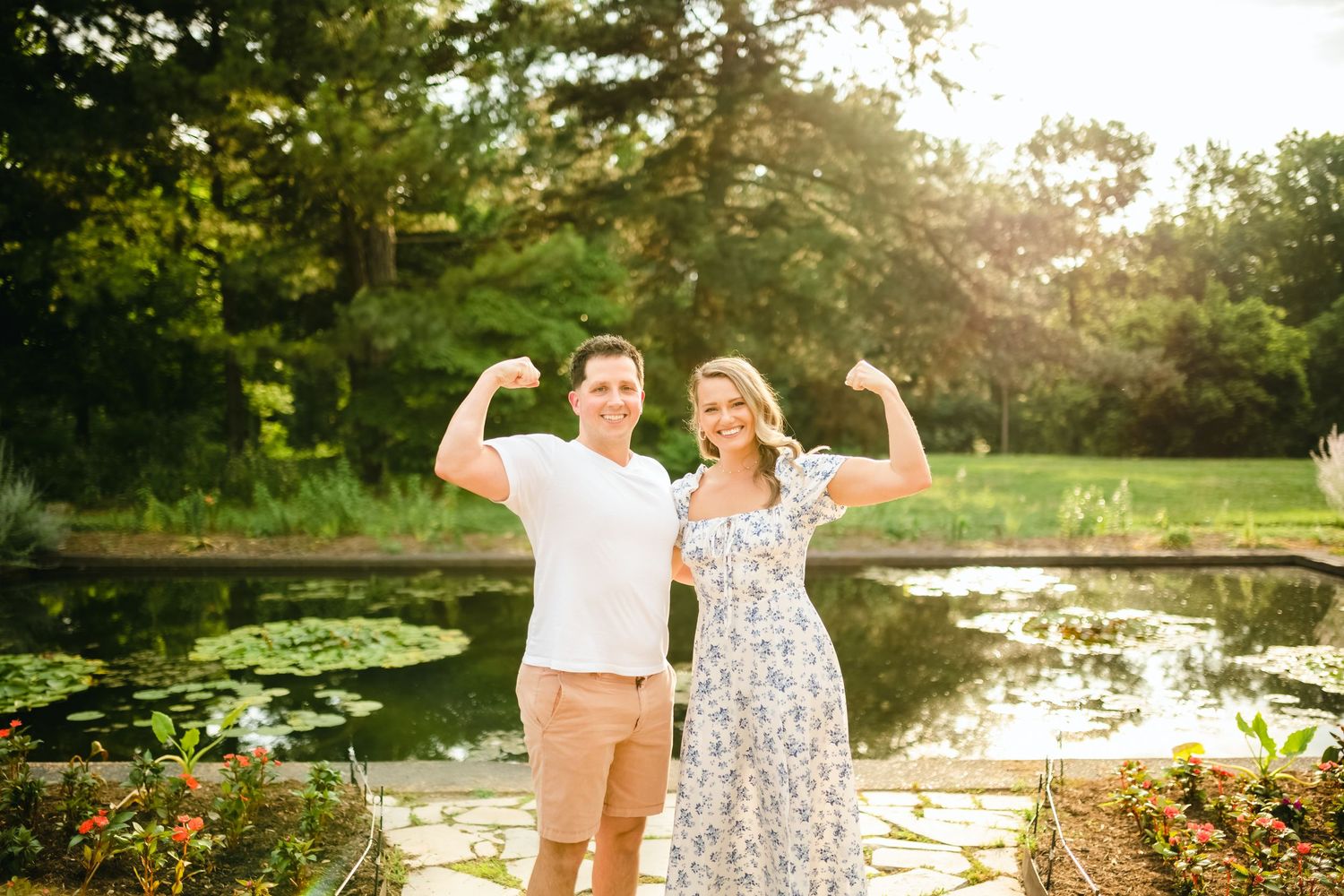 Couple celebrating joyfully by a pond with water lilies at sunset.