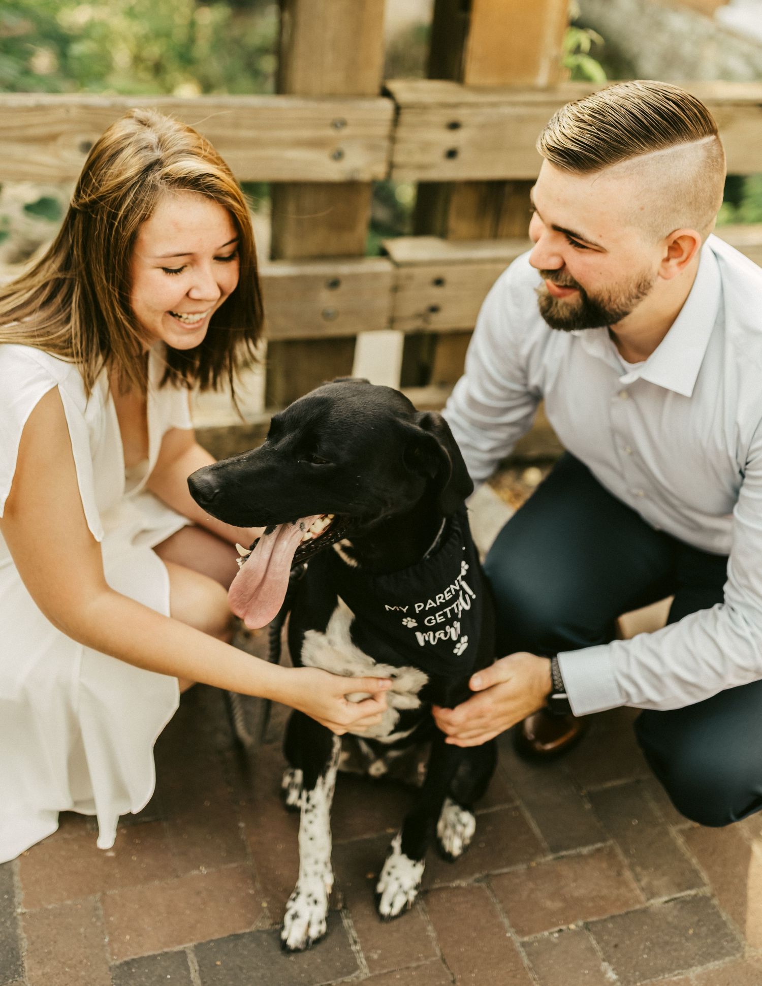 Playful couple interacting with their black and white dog on brick patio.