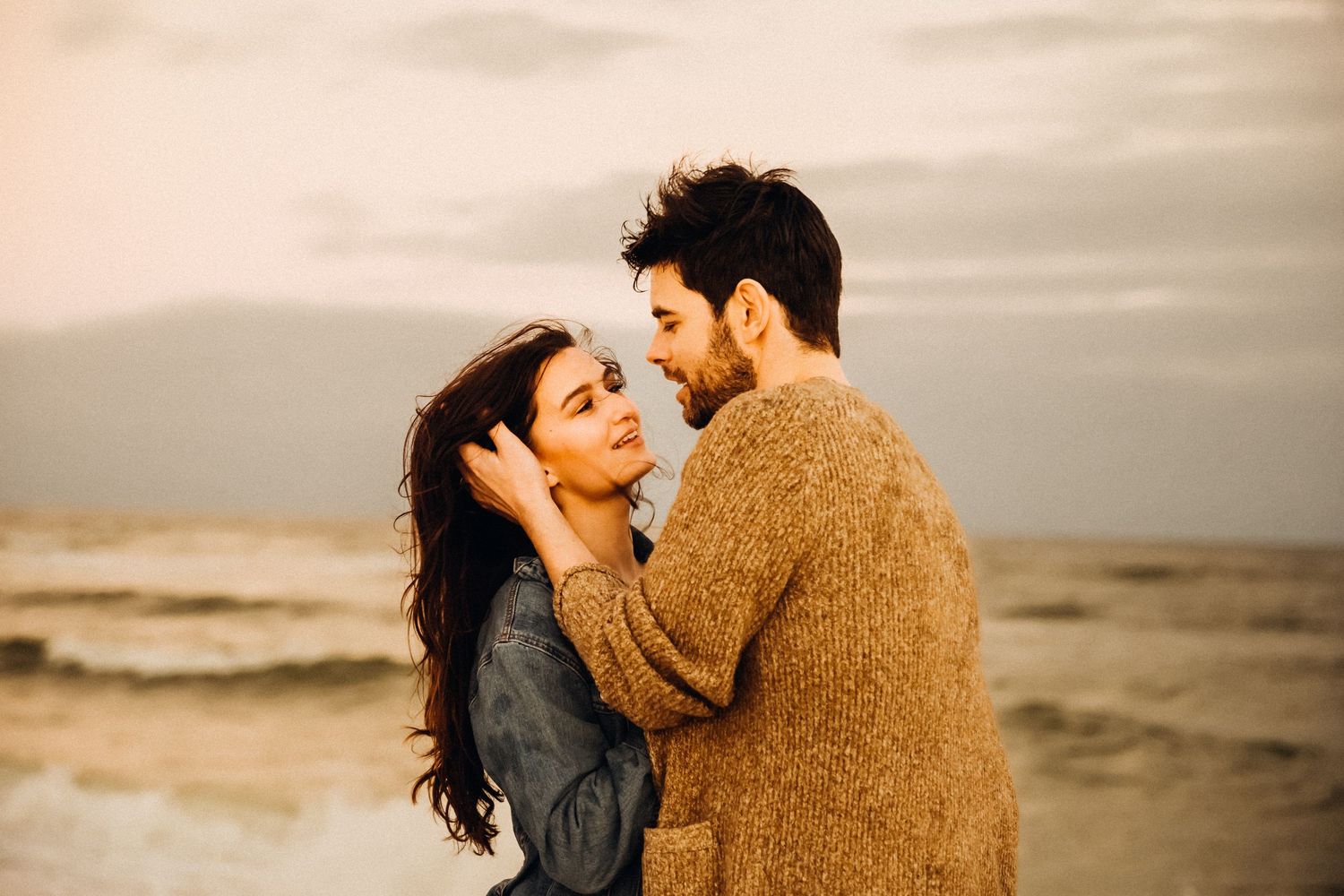 Romantic beach photoshoot during golden hour with ocean waves in background.