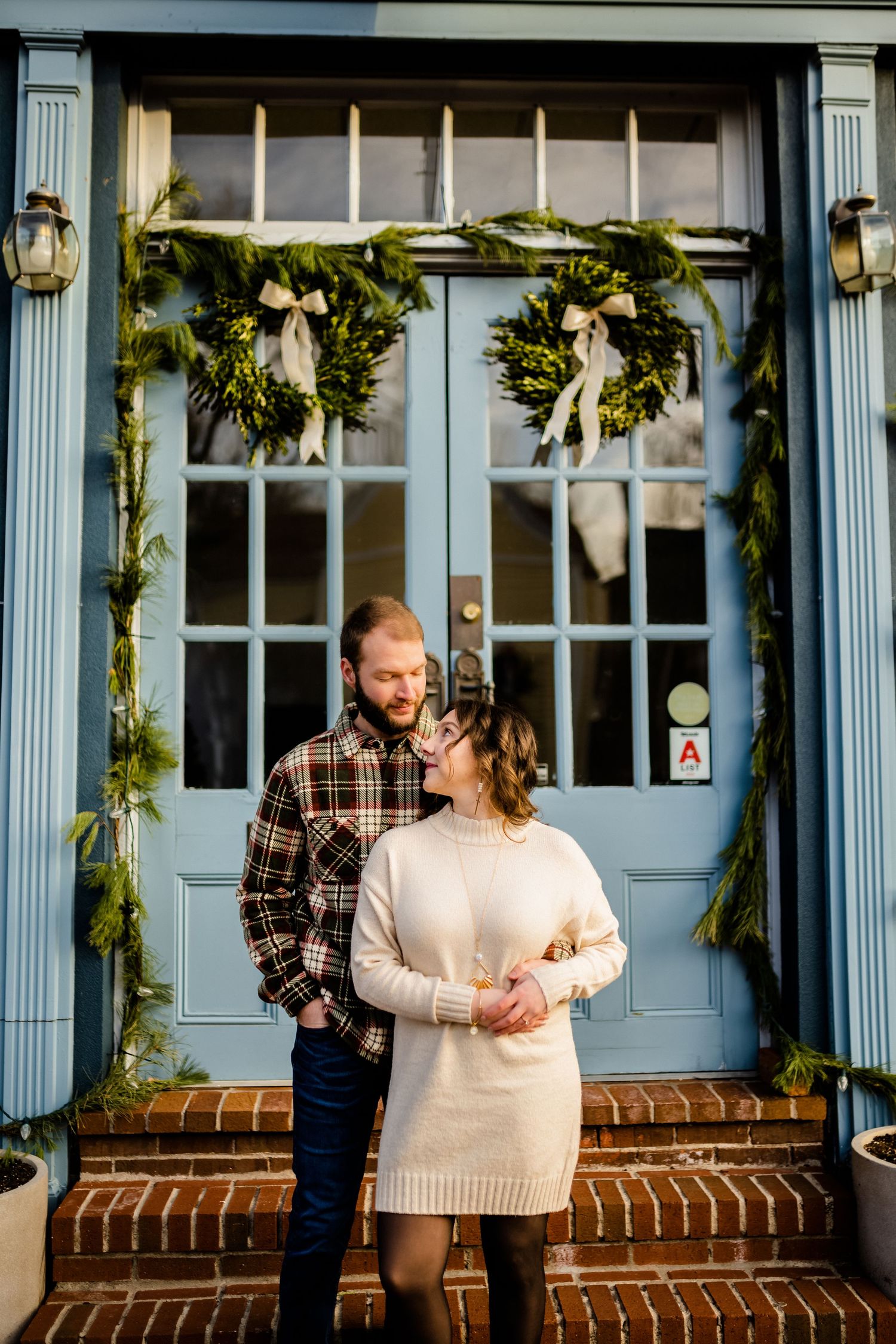 Couple posing in front of a blue historic building decorated with holiday greenery.