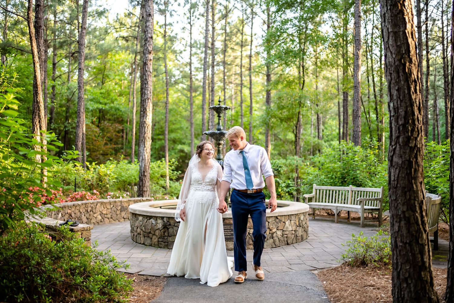 Couple sitting together on a stone wall surrounded by tall pine trees in a romantic forest setting.