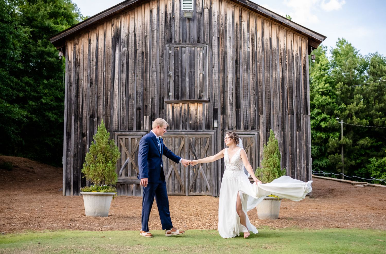 Wedding couple dancing and twirling in front of rustic wooden barn.