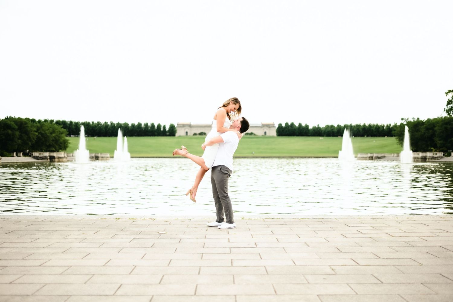 Wedding couple dancing on stone patio near water with sailboats in background.