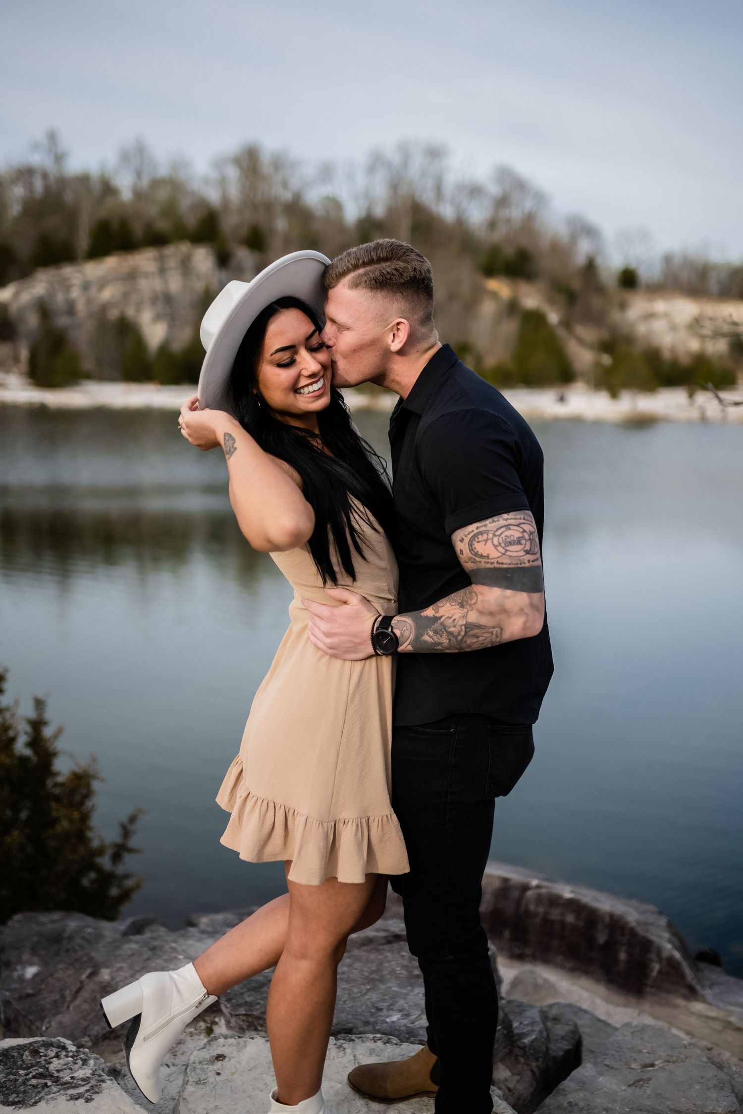 A couple shares intimate moments during their photoshoot on rocky terrain by a serene lake.