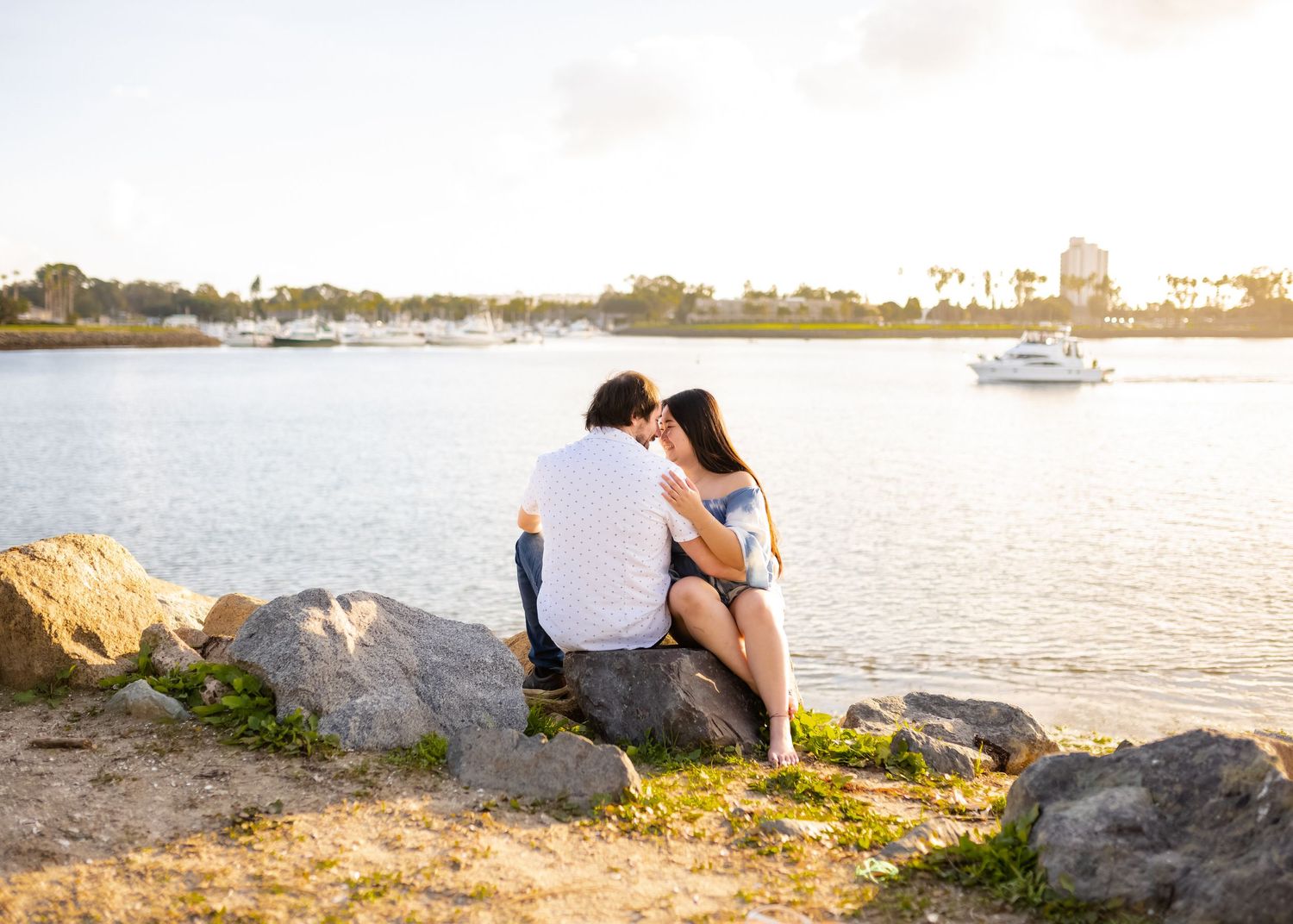 Couple embracing at sunset by the ocean with palm trees in the background.