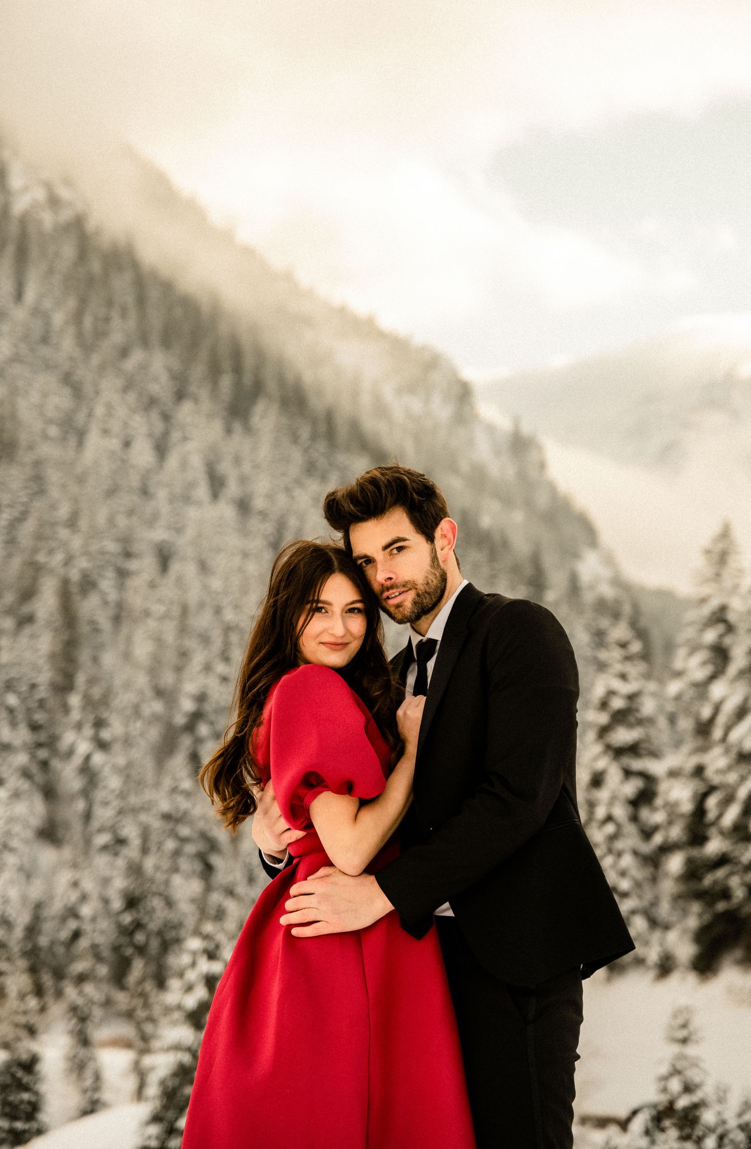 Romantic winter engagement photos with snowy mountains in the background and a red dress.