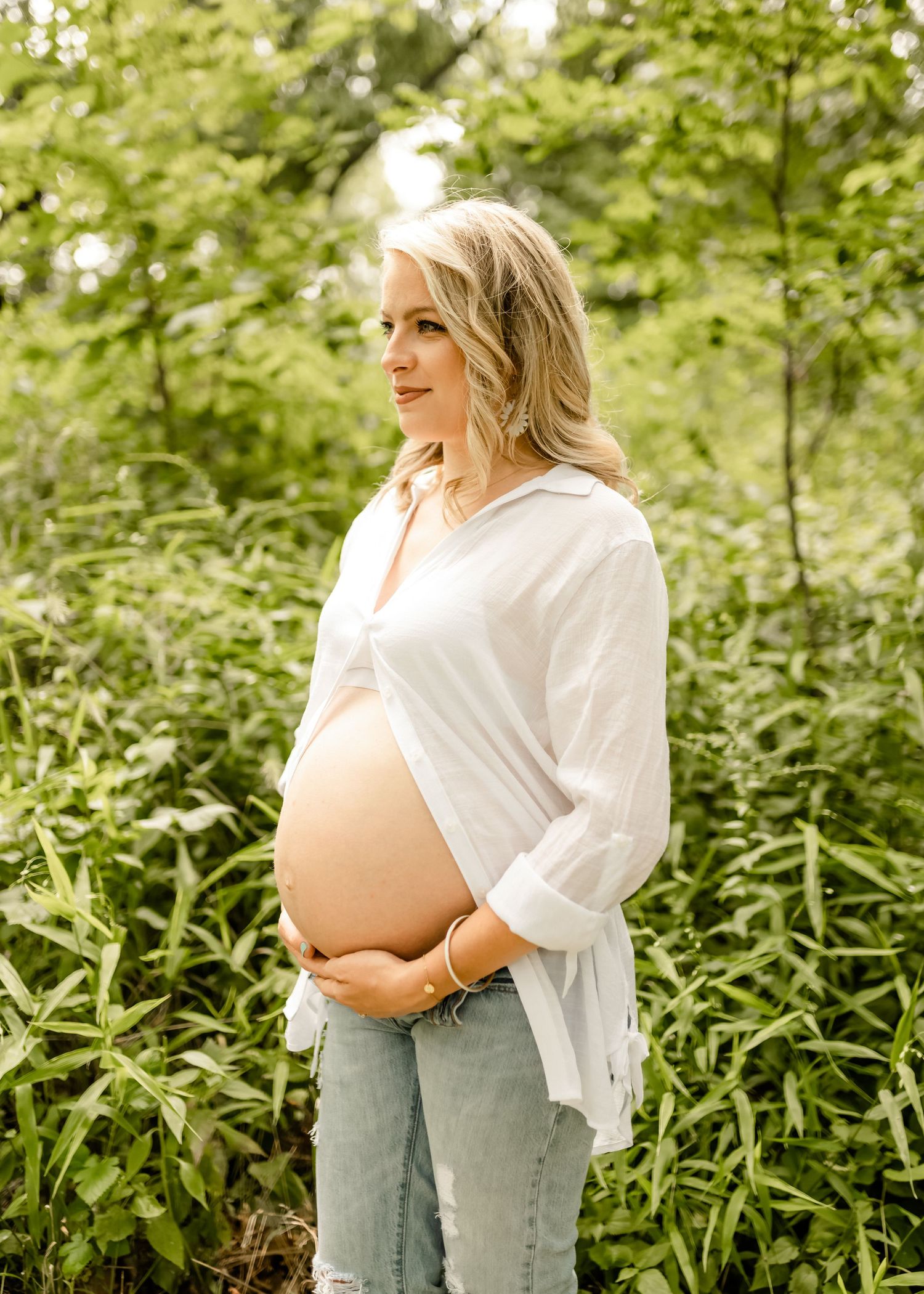 A maternity photoshoot in a lush green outdoor setting shows an expectant mother in casual attire.