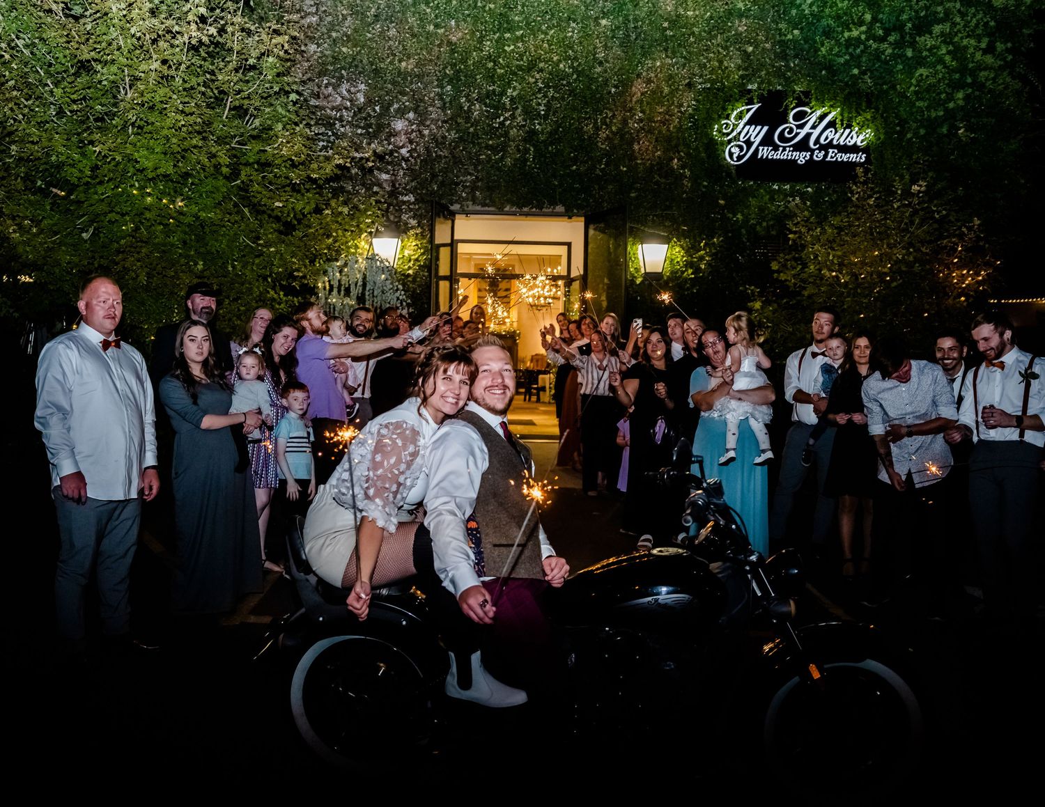 Evening outdoor wedding reception with guests gathered under string lights.