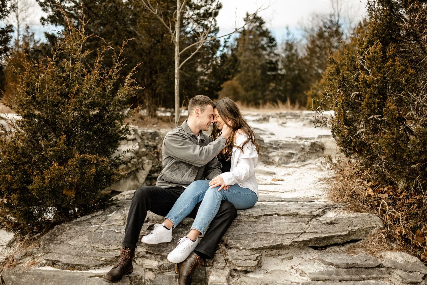 Romantic couple embraces on rocky cliff edge during sunset photoshoot in natural outdoor setting.