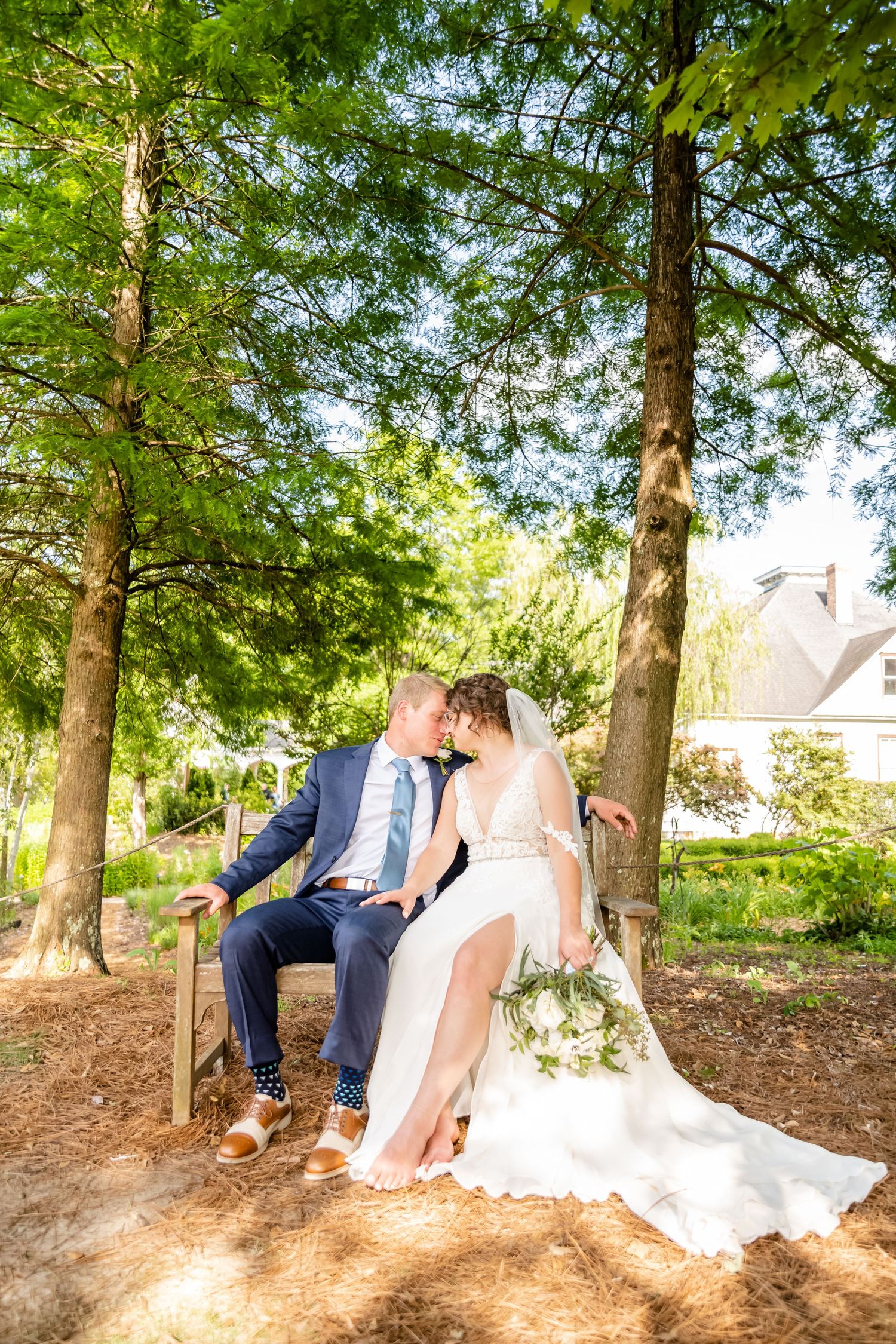Romantic forest scene with couple sitting on stone wall under tall trees and dappled sunlight.