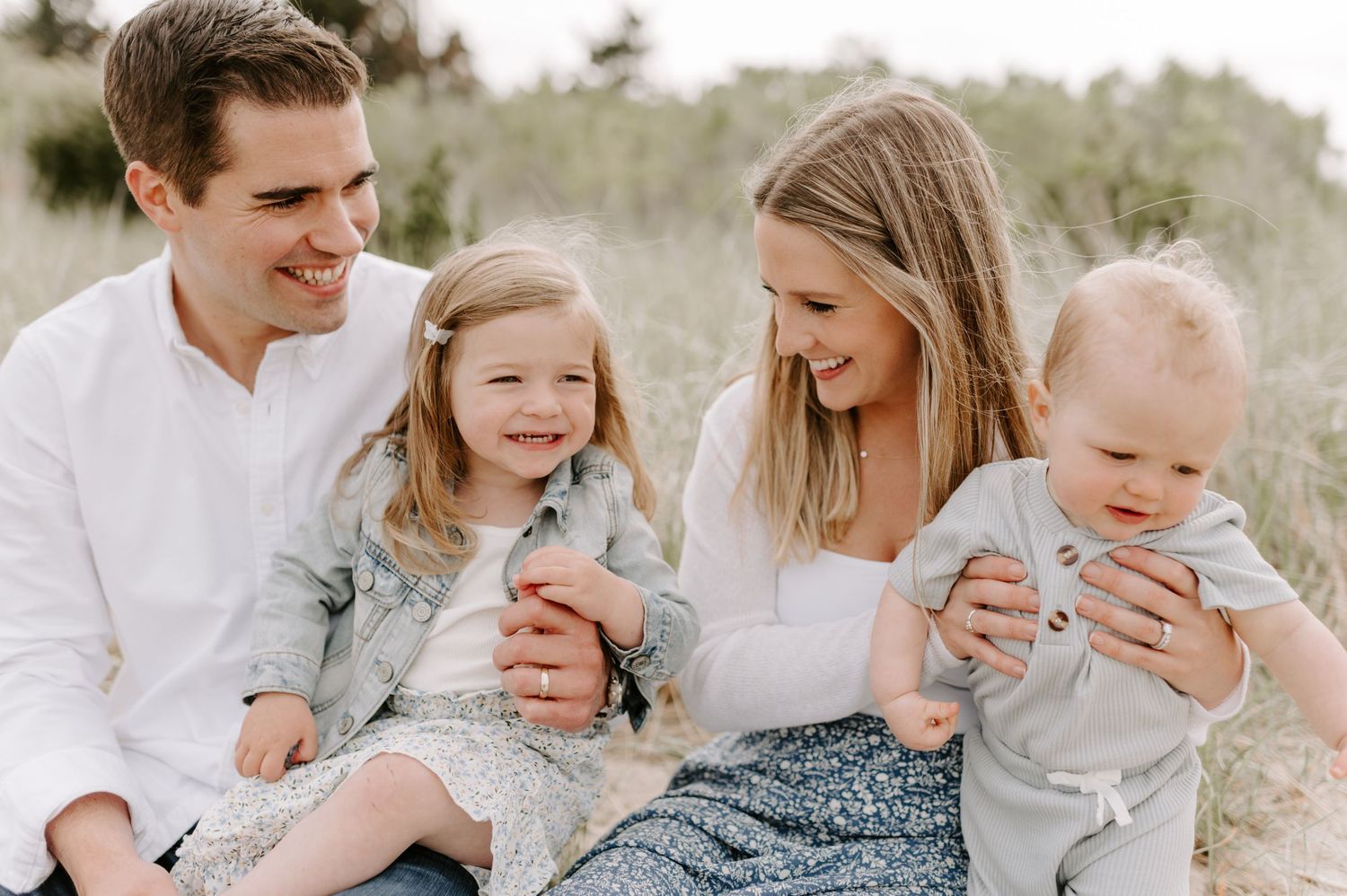 Family sitting together on a grassy hill during an outdoor photo session.