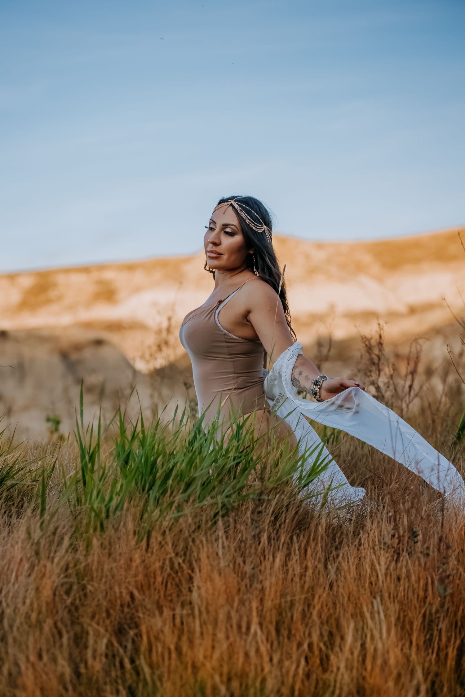 Woman in tan top dancing with fabric in golden field at sunset.