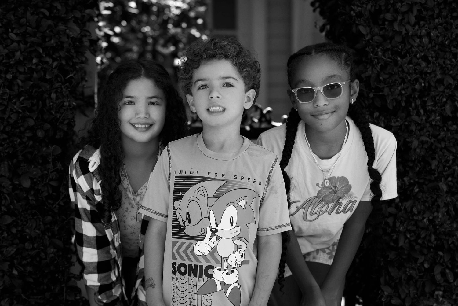 Three friends posing together against a hedge wall.