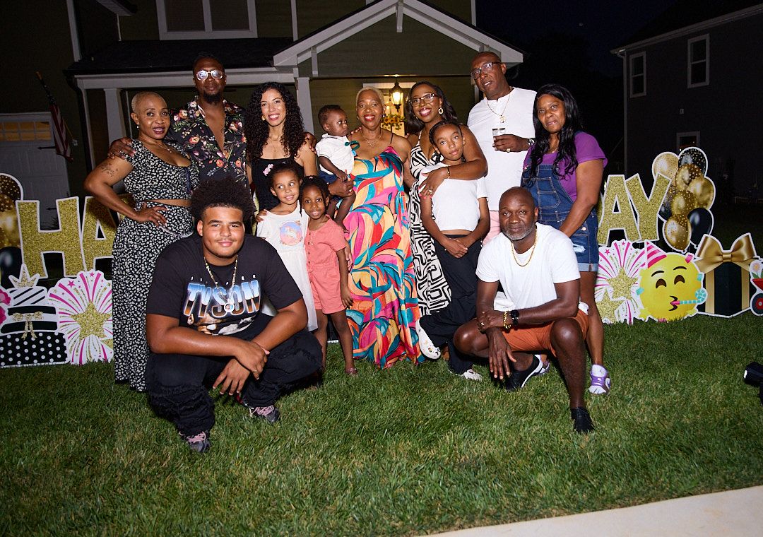 Large group photo at an outdoor party with decorative yard signs visible in background.