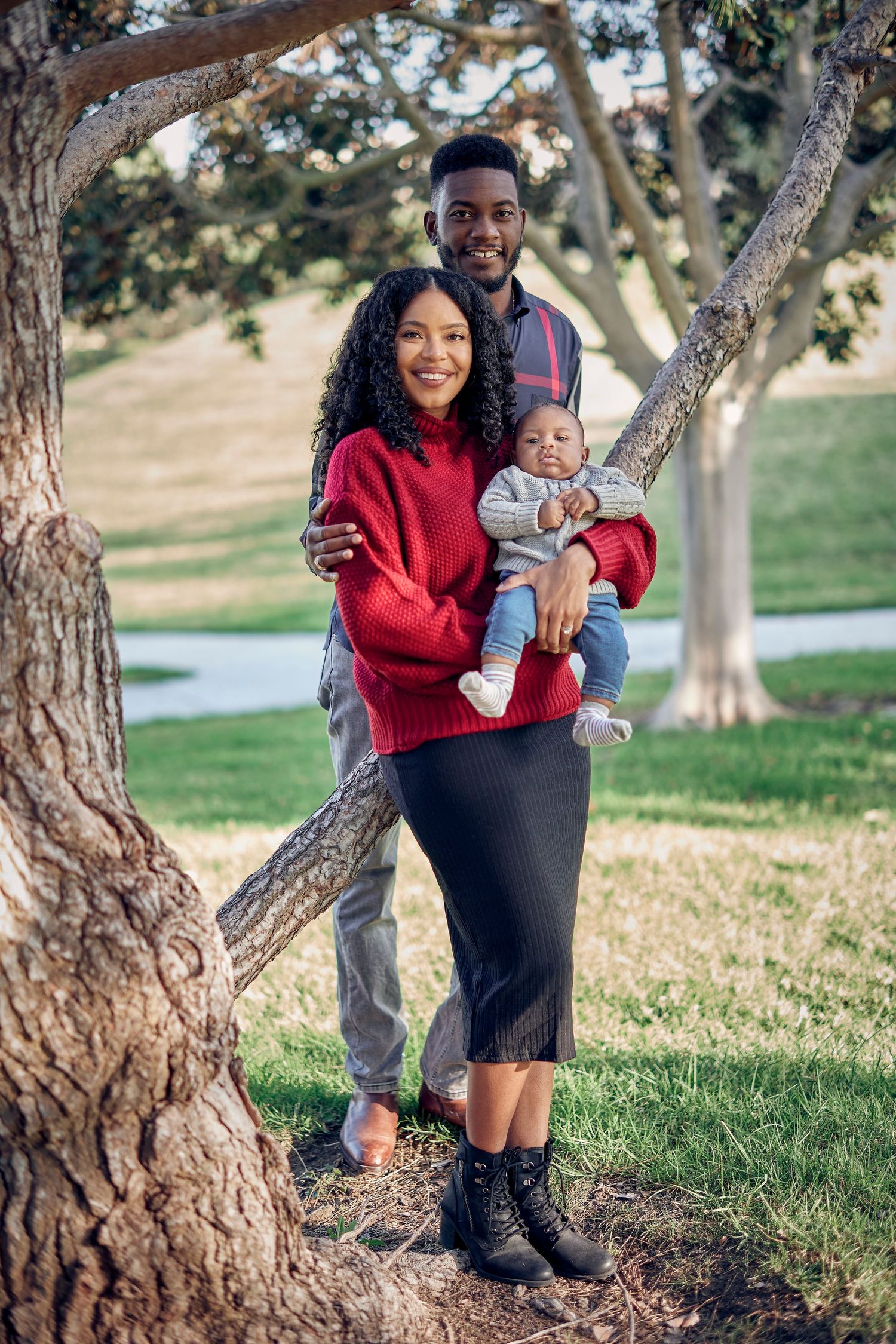 A family poses together near a tree trunk in a park setting.