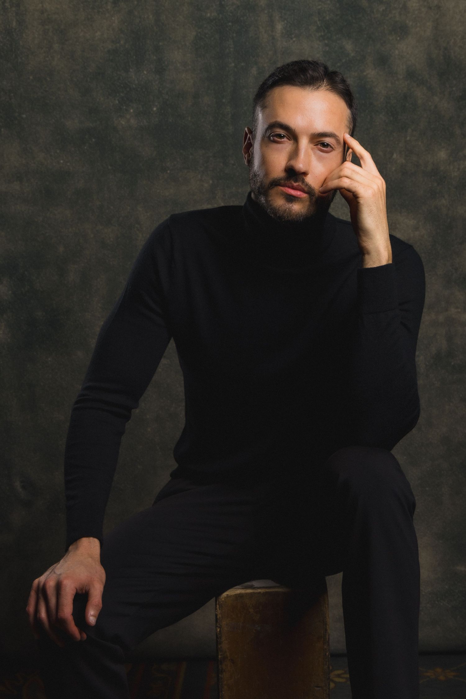 Moody portrait of a man in black sweater sitting thoughtfully against dark background. Shot by Mika Larson Photography.