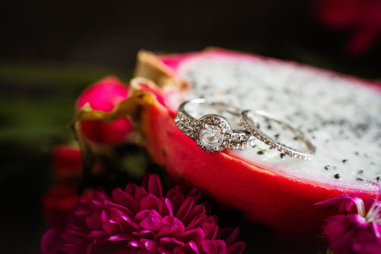Diamond engagement ring on dragon fruit with pink flowers in soft focus.