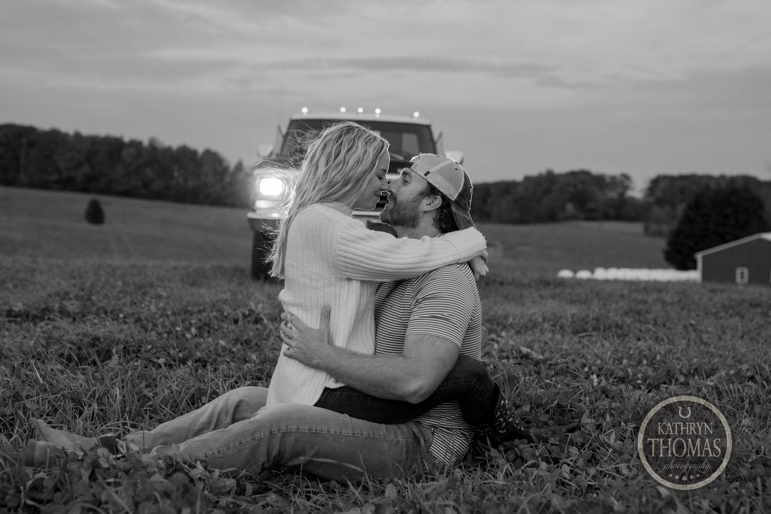 Black and white photo of a couple sharing an intimate moment in a country field at dusk.