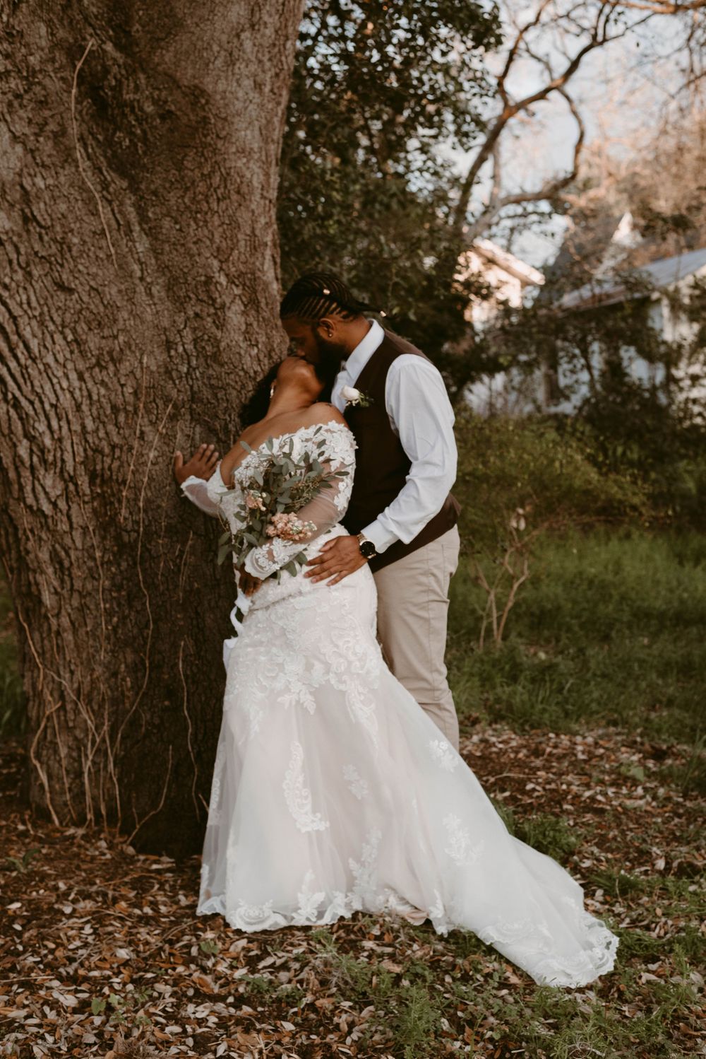Intimate wedding portrait with couple embracing by a large tree in a dreamy outdoor setting.