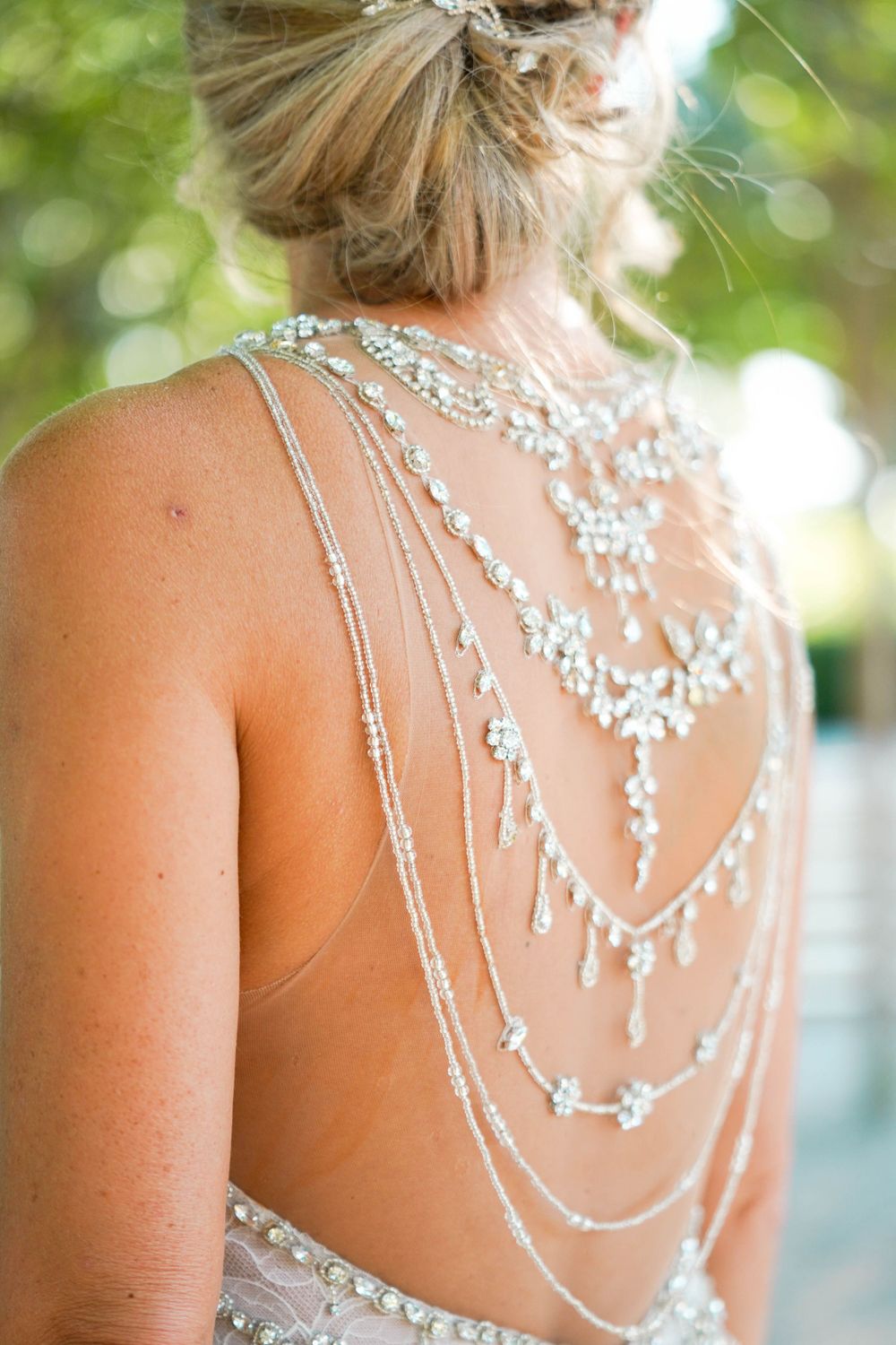 Intricate beaded back detail of a wedding dress with delicate crystal chains against soft bokeh background.