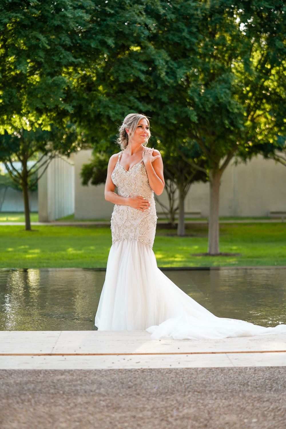 Elegant wedding dress with lace detail and flowing train photographed by a reflecting pool.