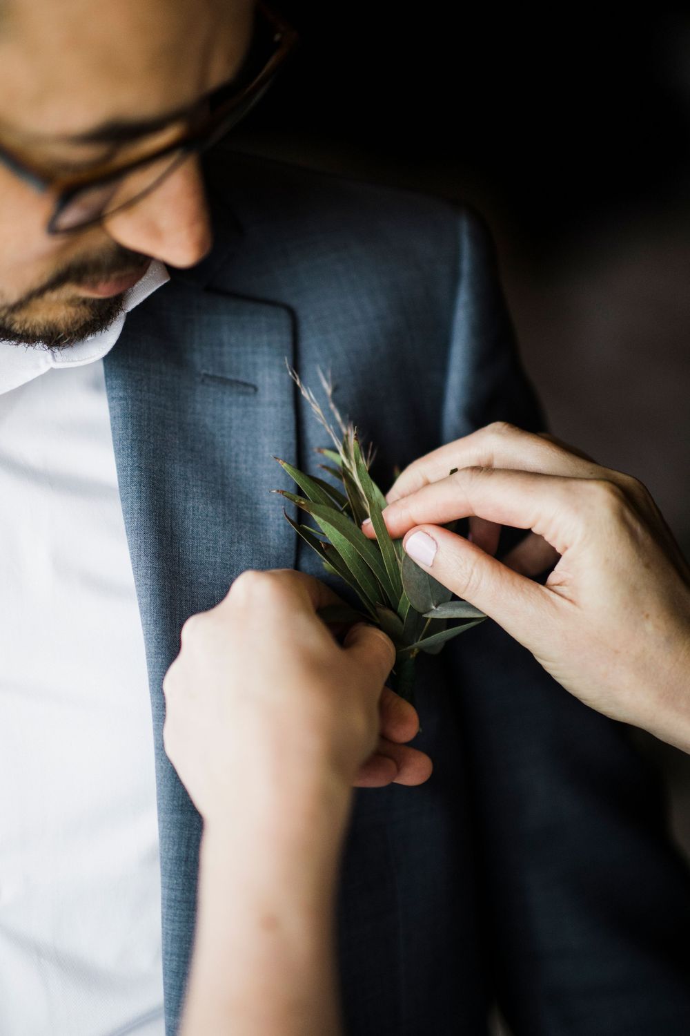 Hands pinning a delicate green boutonniere onto a navy suit jacket lapel.