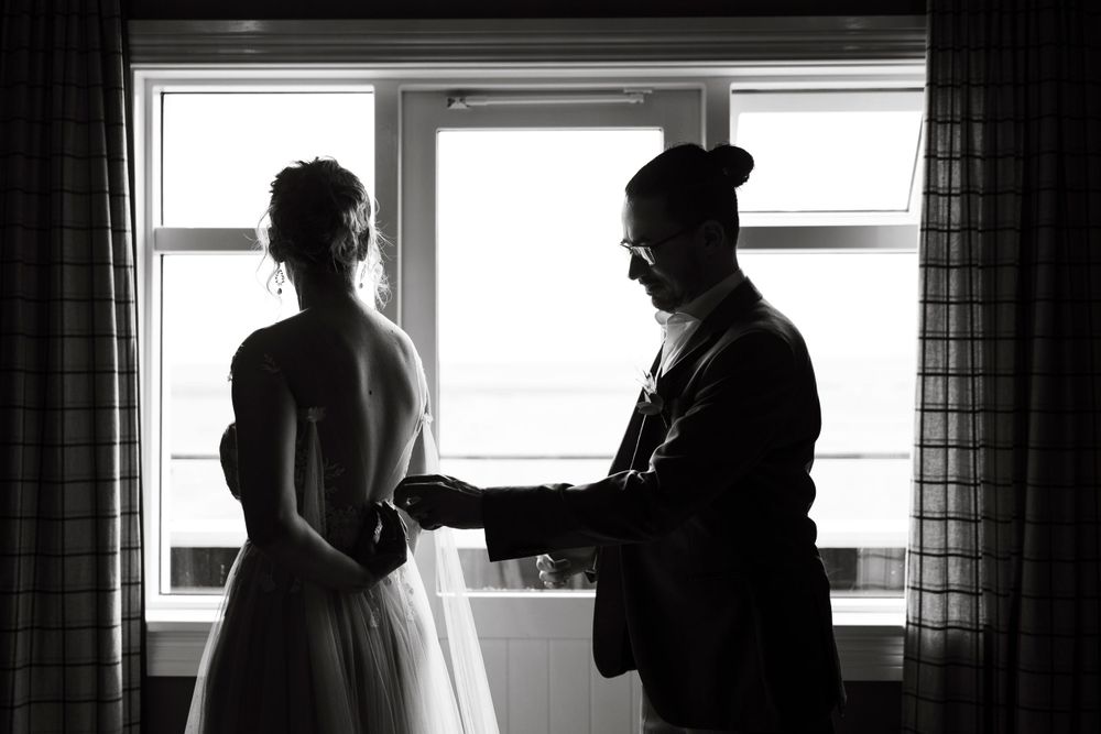 Silhouetted figures by window during intimate indoor wedding preparation.