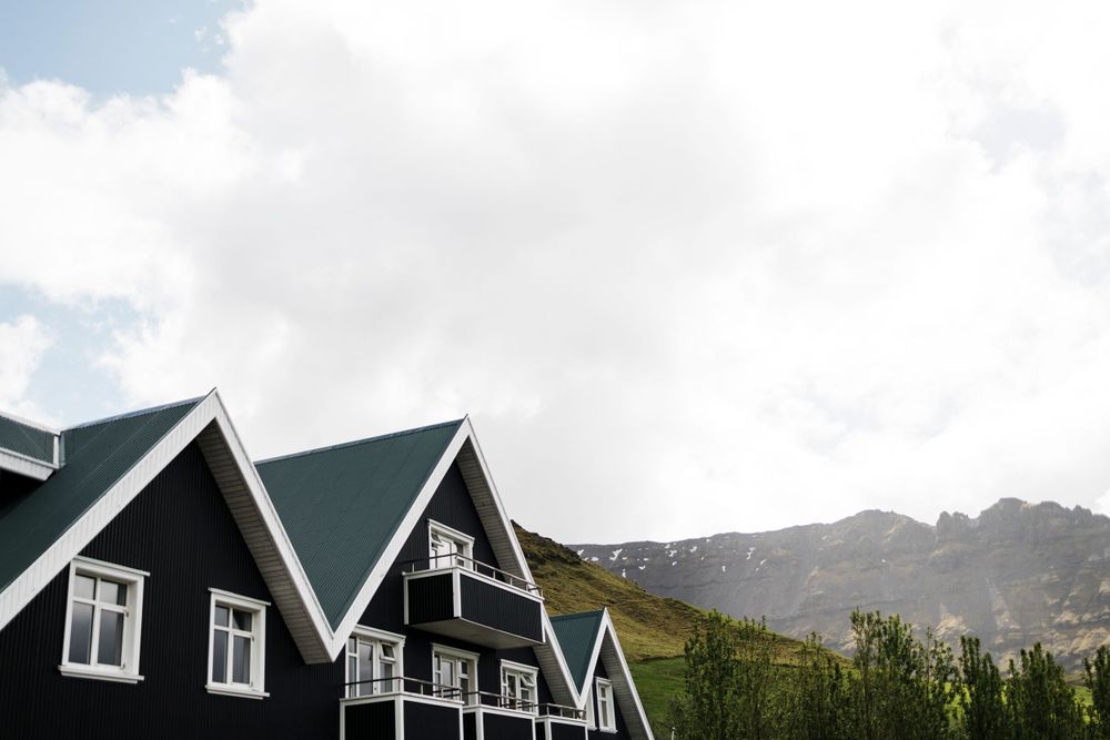 Row of traditional black Scandinavian houses with white trim against mountain backdrop.