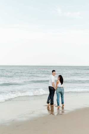 A couple stands ankle-deep in ocean waves on a serene beach.