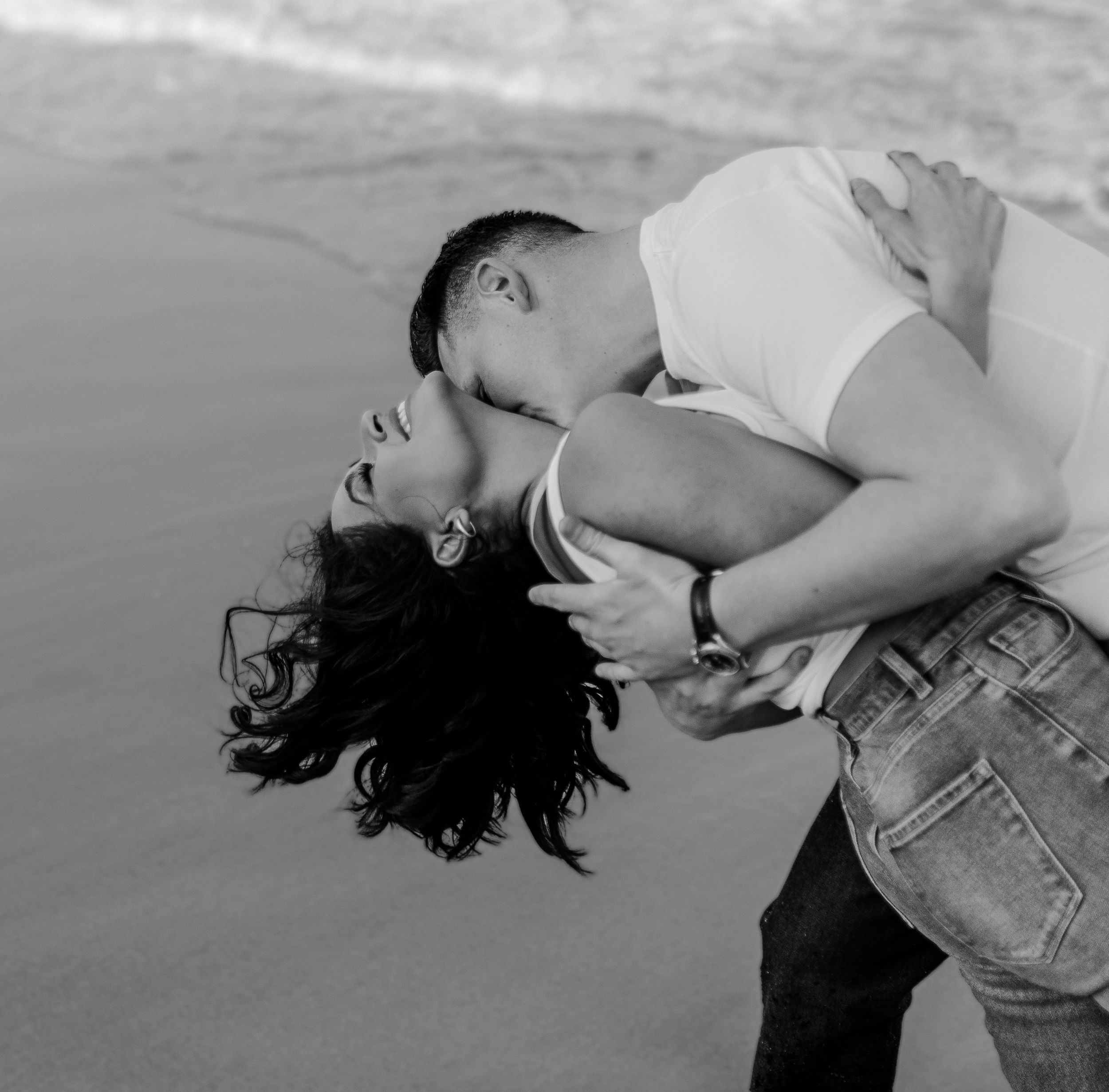 A romantic black and white portrait of a couple embracing on the beach.