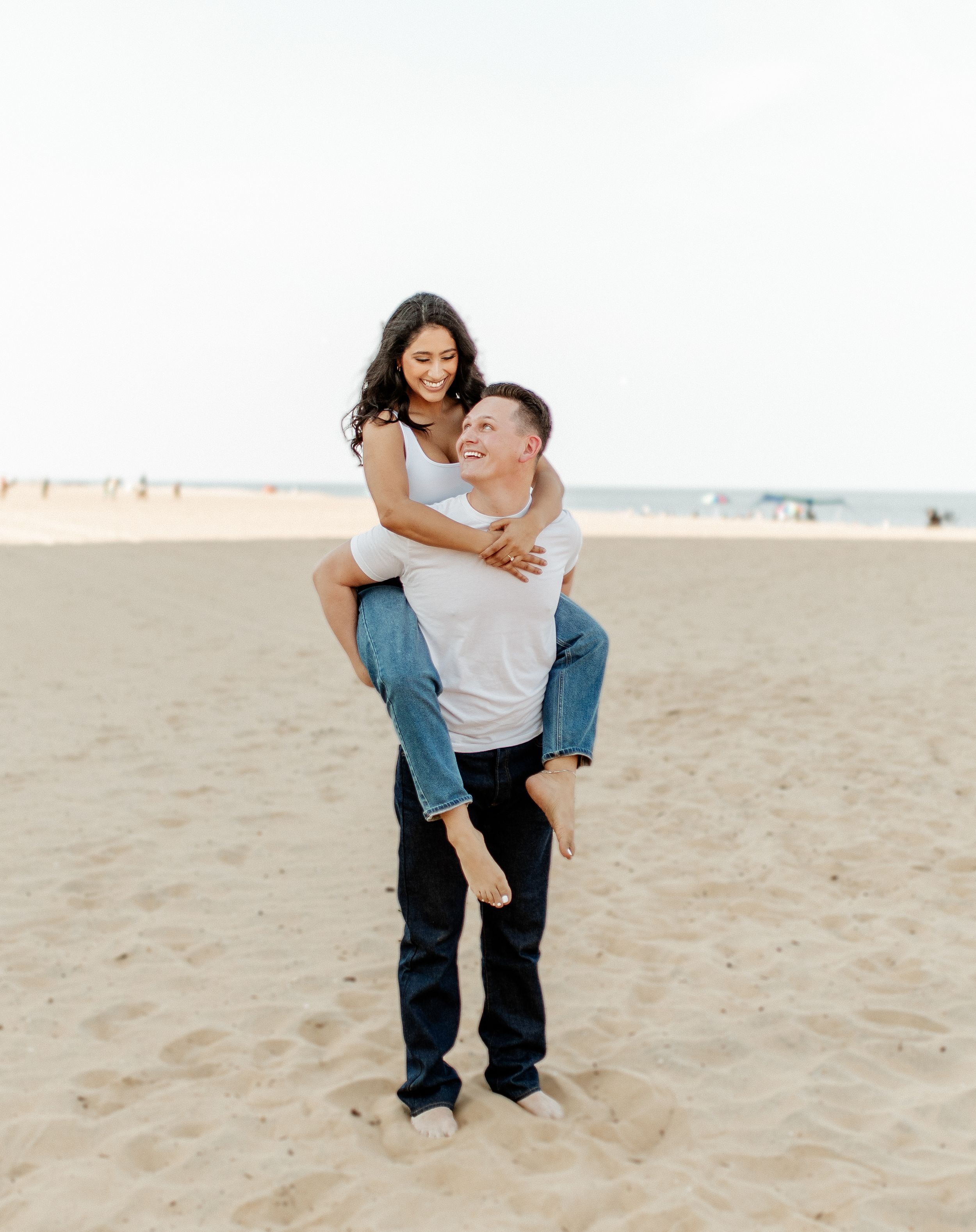 A playful piggyback ride on a sandy beach during a couples photoshoot.