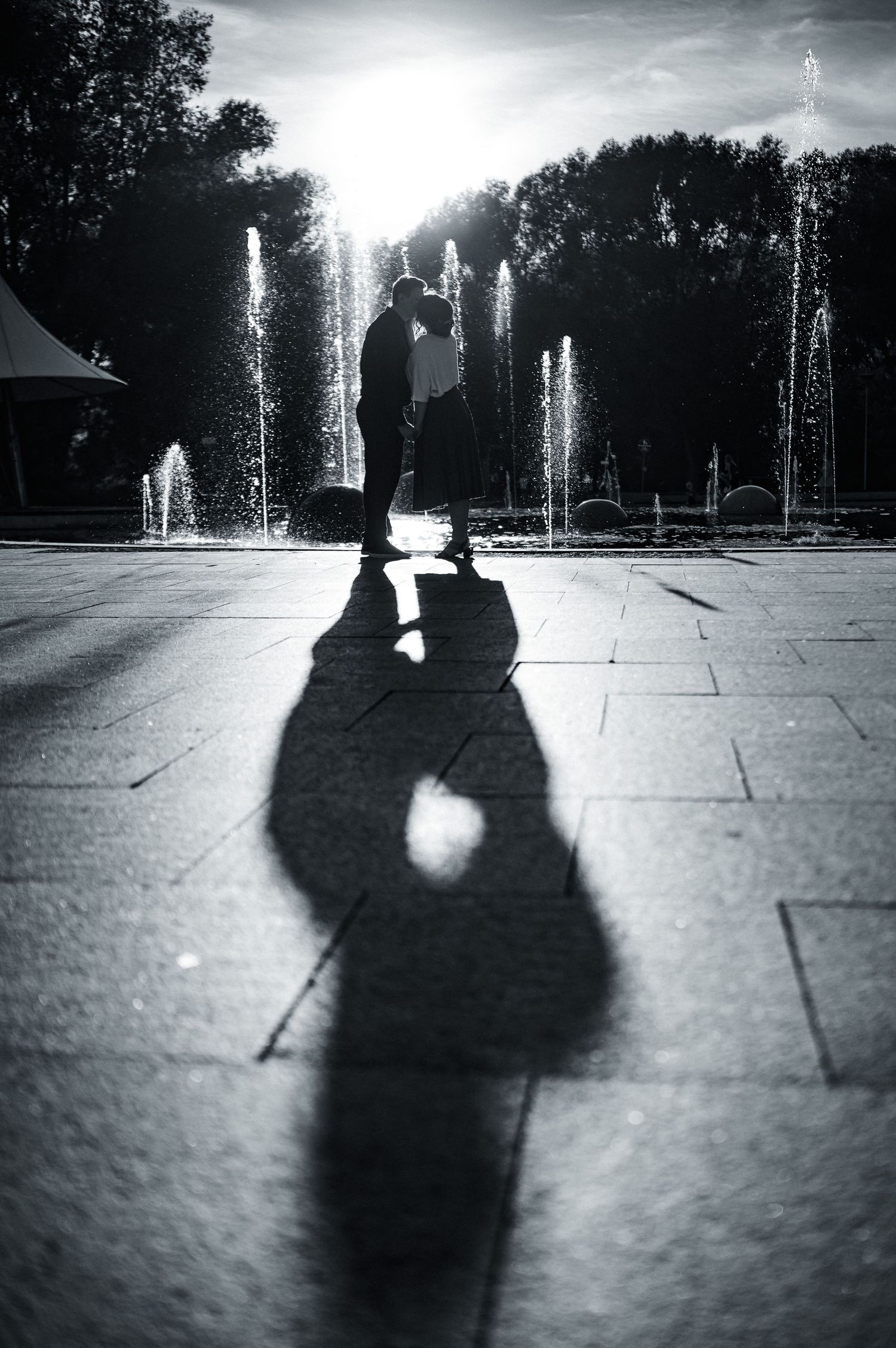 Black and white silhouettes of couple dancing with water fountains in background.