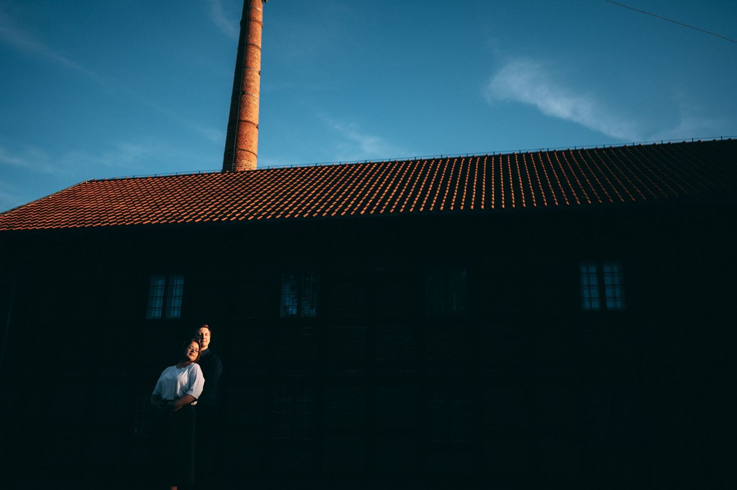 Industrial brick building with tall chimney photographed at sunset against blue sky.