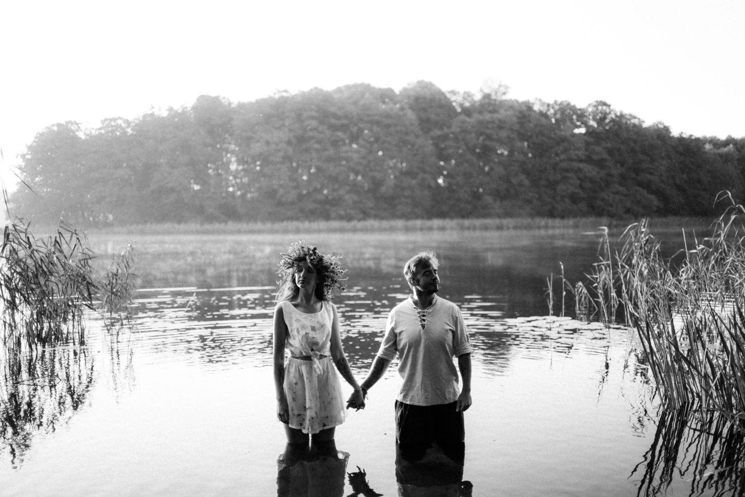 Black and white lakeside scene with tall reeds and tranquil water.