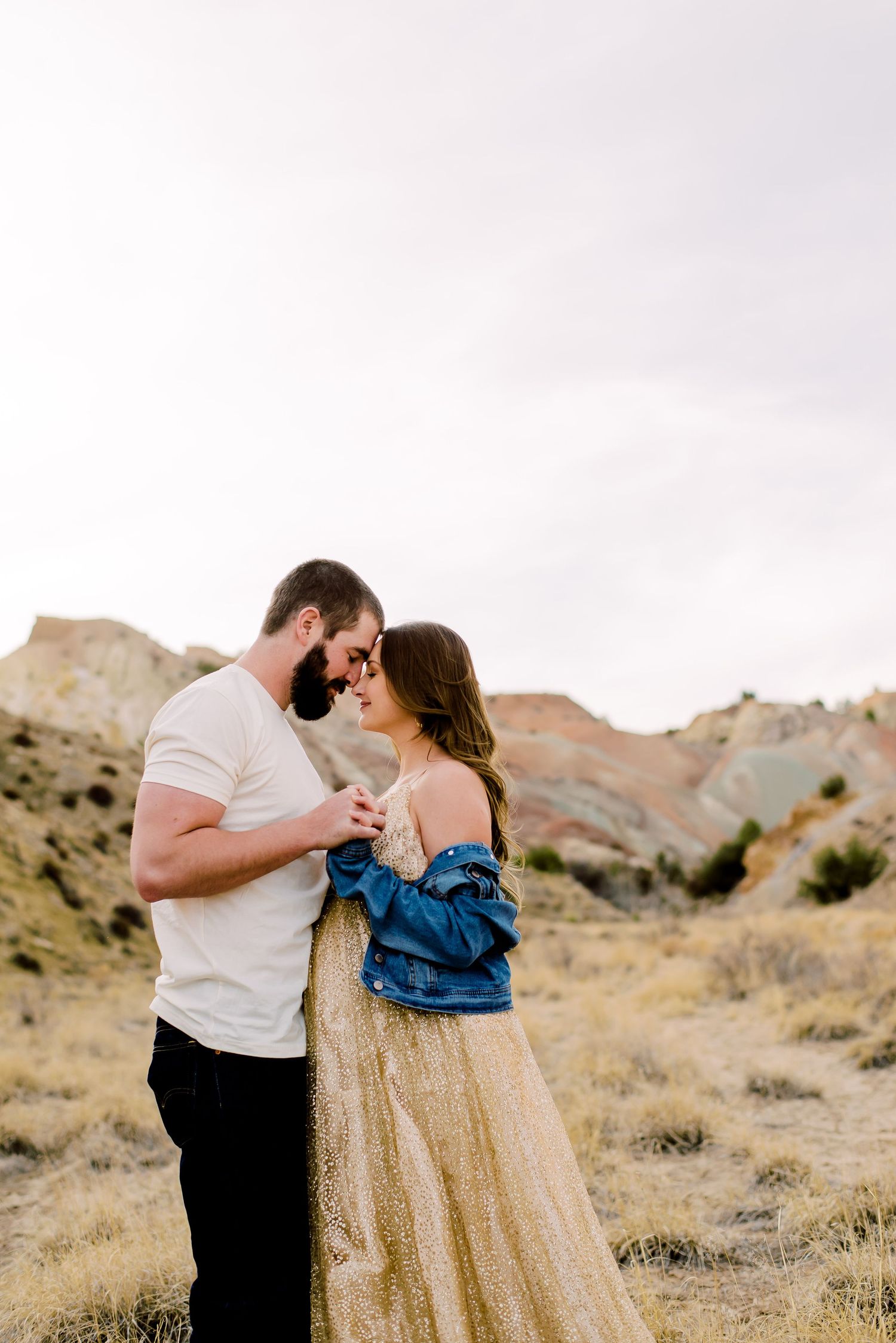 Couple sharing a romantic moment in a golden desert landscape, woman in sequin dress and denim jacket.