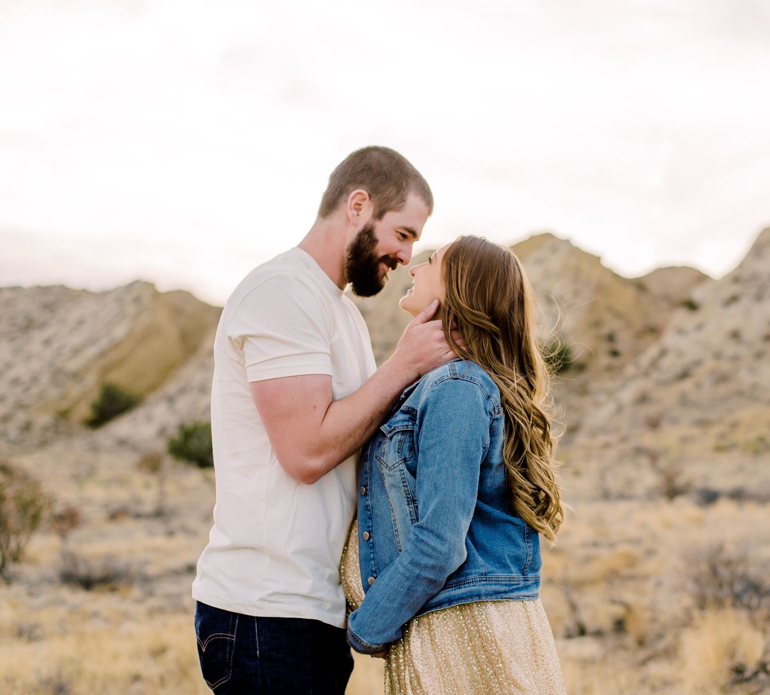 Couple sharing a romantic moment in a desert landscape, man in white tee and woman in denim jacket.