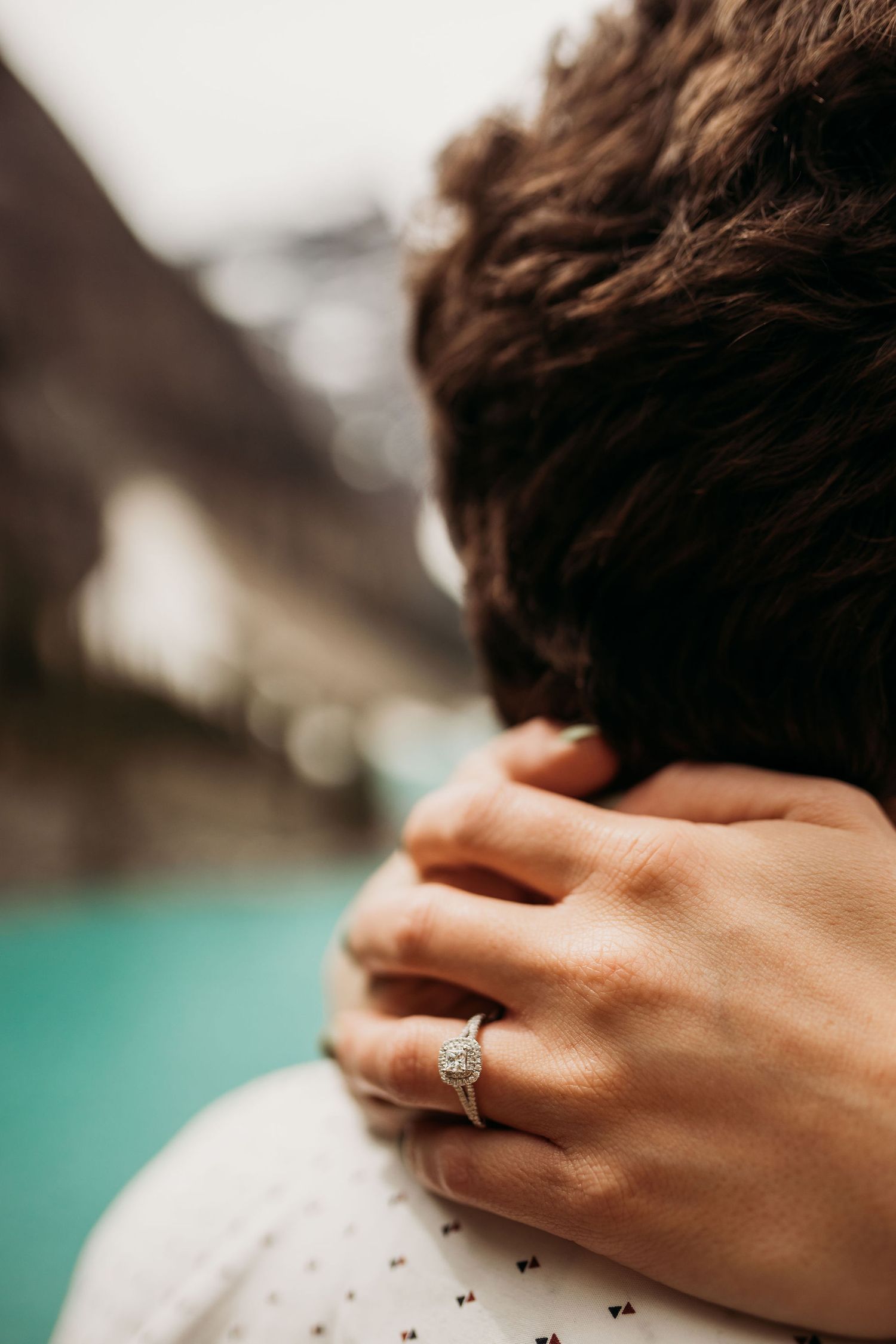 Close-up shot of engagement ring worn on hand with mountain scenery in background.