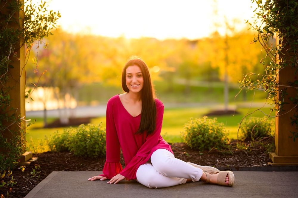 A sunset portrait session featuring a red sweater and white pants on a garden pathway.