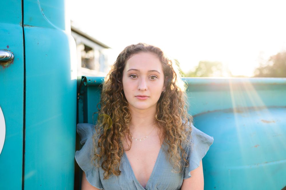 A golden hour portrait against a turquoise wall with natural sunlight and lens flare.