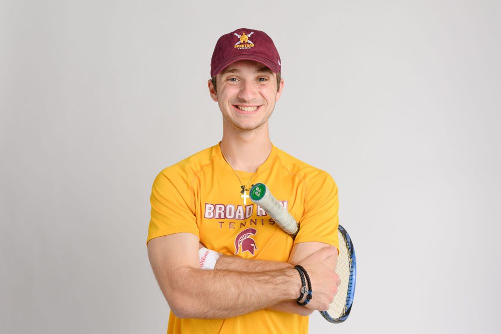 A person in a yellow t-shirt with a sports logo smiles while wearing a red baseball cap.