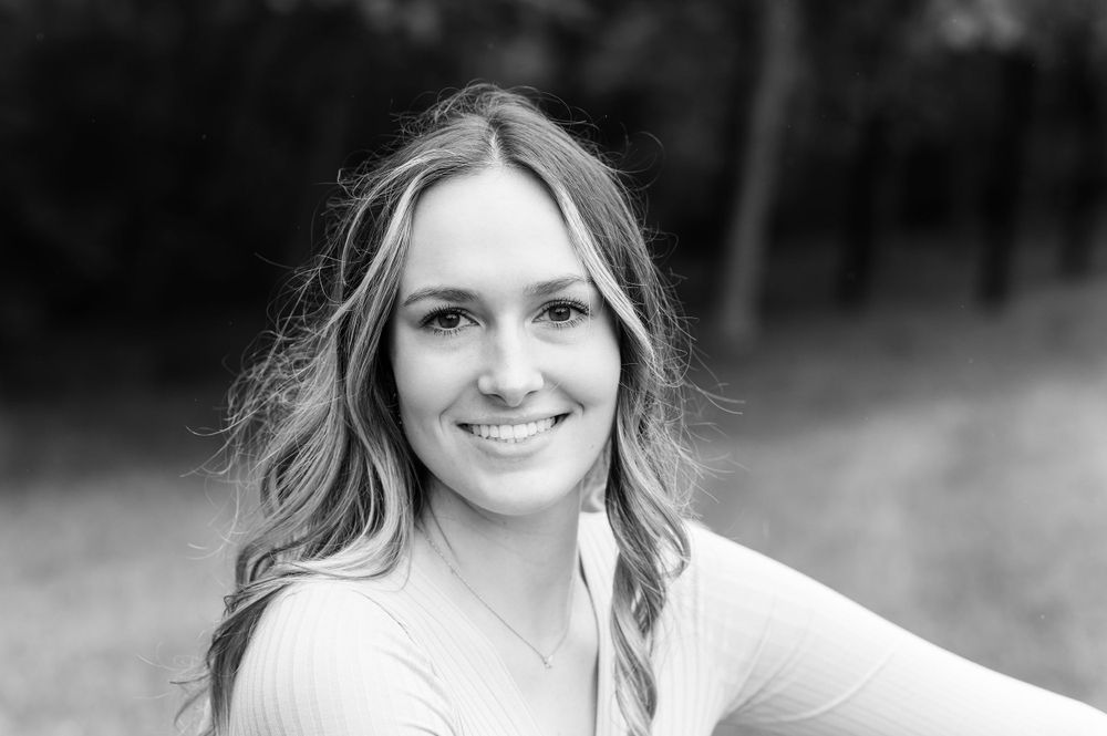 A black and white portrait of someone with wavy blonde hair and a bright smile.