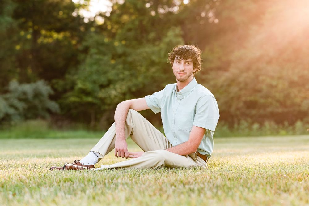 A person in casual attire sits on grass during sunset.