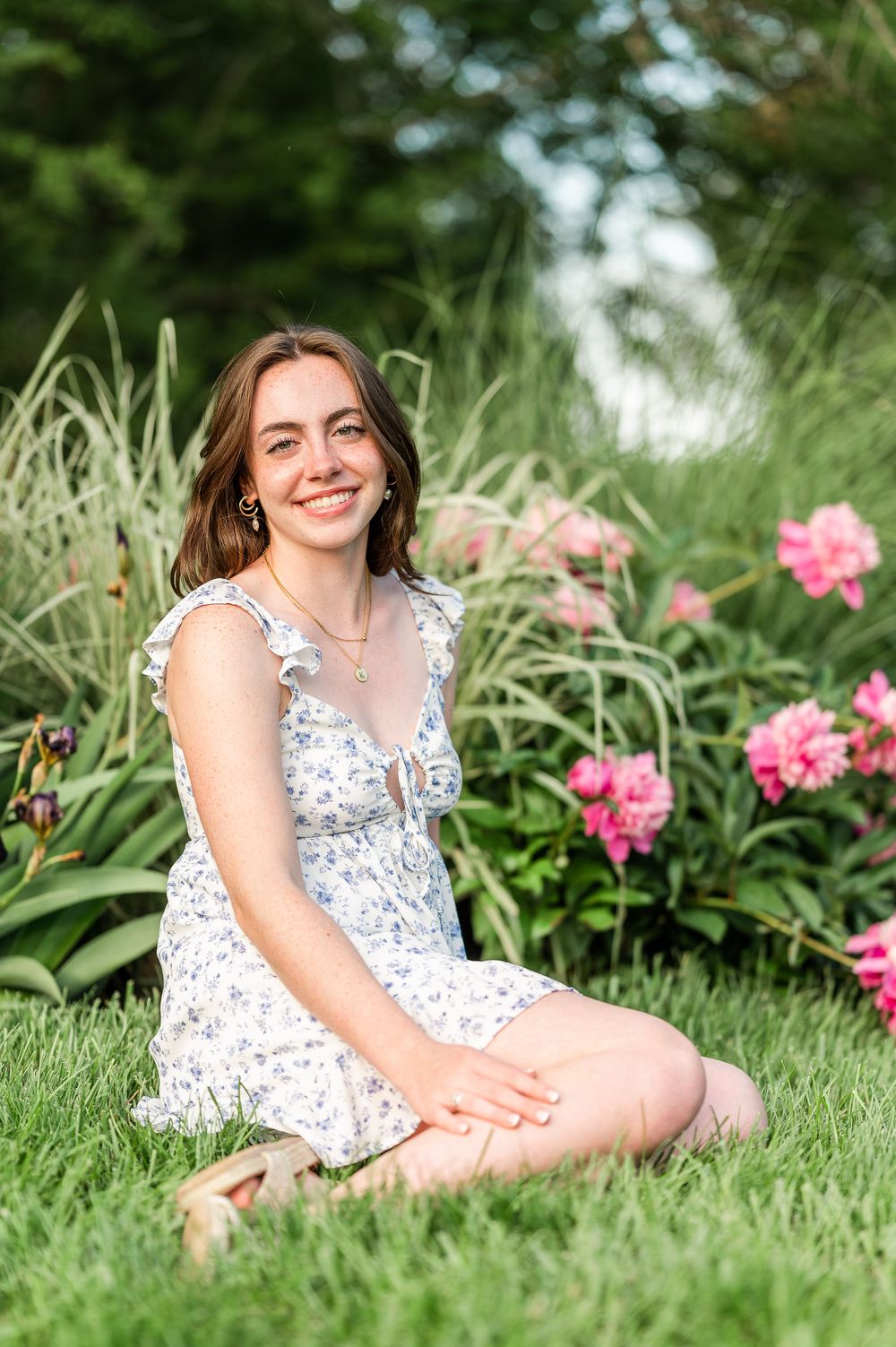 A person in a white floral dress sits gracefully among blooming pink flowers in a garden.