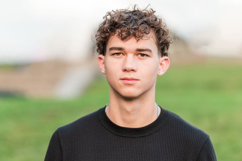 Portrait of person in black ribbed sweater against outdoor background.