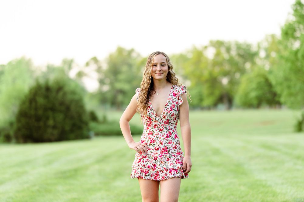 Person in a floral summer dress poses in a sunlit green park.