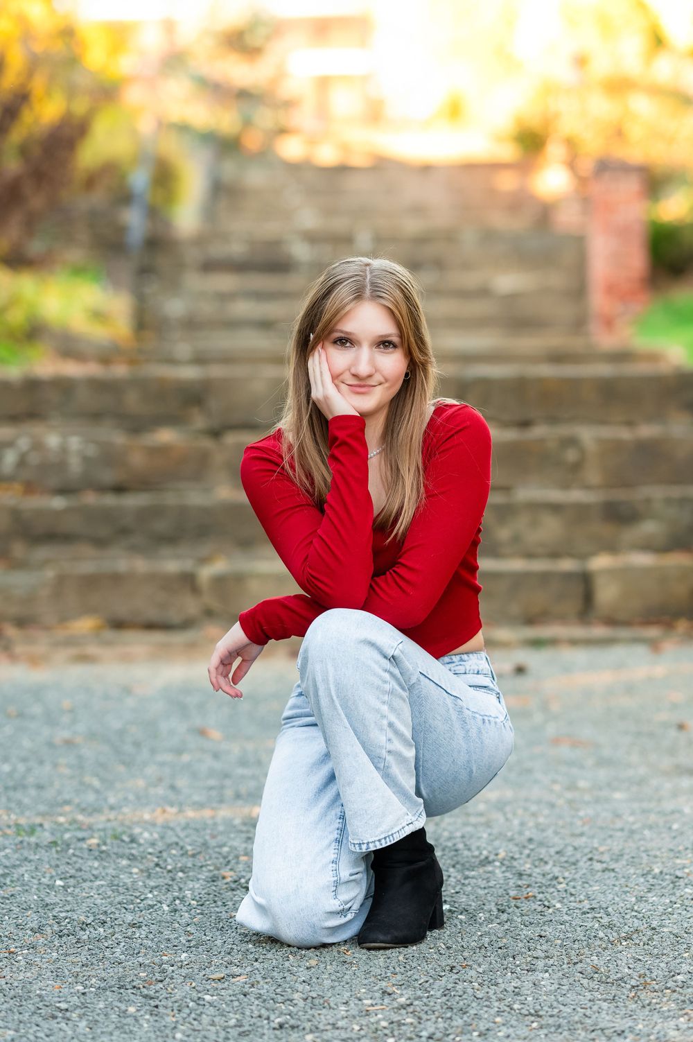 Casual portrait of someone in a red sweater sitting on stone steps during golden hour.